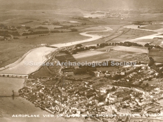 z89.989 View of town c1921 Aerial view over Shoreham-by-Sea looking north west with River Adur in foreground and South Downs with Chanctonbury Ring in distant background. Footbridge visible in foreground, railway bridge on left and old toll bridge in middleground with Lancing College and Chapel to its left. Catholic church in foreground centre left, St Mary de Haura centre right with Shoreham Grammar school in Pond Road behind the tower of St Mary's. River Adur winding through fields into distance.